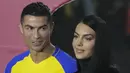 Cristiano Ronaldo menatap sang kekasih Georgina Rodriguez saat mereka menghadiri upacara penyambutan dirinya sebagai pemain baru Al Nassr di Stadion Mrsool Park, di ibu kota Saudi, Riyadh, Selasa (3/1/2023). Kekasih CR7 yang biasanya kerap memamerkan kemolekan tubuhnya terlihat lebih sopan dalam berpakaian. (AP Photo/Amr Nabil)