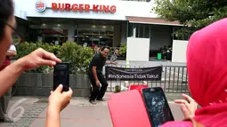 Warga berfoto di dekat poster #Indonesiatidaktakut yang dipasang di depan Menara Cakrawala, Jakarta, Sabtu (16/1). Lokasi teror di kawasan Sarinah Thamrin terus didatangi warga untuk mengabadikan diri atau foto selfie. (Liputan6.com/Faizal Fanani)