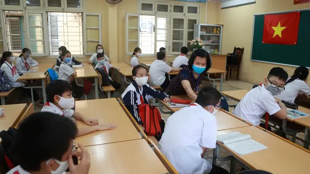 Seorang guru memeriksa suhu murid-muridnya sebelum memulai kelas di sekolah menengah Dinh Cong di Hanoi pada hari Senin. Siswa di seluruh Vietnam kembali bersekolah setelah tiga bulan belajar online.
