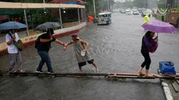 Seorang kernet (tengah) membantu penumpangnya menyebrangi genangan air di Manila, Filipina, Kamis (27/7). Pihak Atmosfer, Geofisika dan Astronomi Filipina (PAGASA) membenarkan adanya badai tropis ‘Nesat’ di timur laut Filipina. (AP/Bullit Marquez)