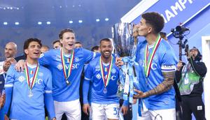 Gelandang Napoli, Scott McTominay (kedua dari kiri) melihat rekan setimnya, Giovanni Di Lorenzo, mencium trofi juara Piala Super Italia 2025 di King Al-Awwal Park Stadium, Riyadh, Selasa (23/12/2025) dini hari WIB. (Fayez NURELDINE / AFP)