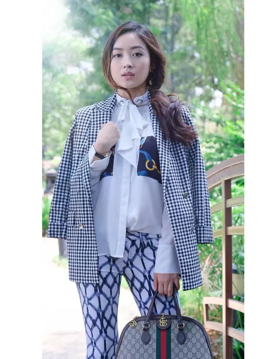 Natasha Wilona tampil berani dengan tabrak motif pada tampilan monokromnya. Kemerja berpita putih dengan saku print dipadukan dengan celana print. Dengan low ponytail, penampilan Natasha Wilona diakhiri dengan blazer kotak-kotak.