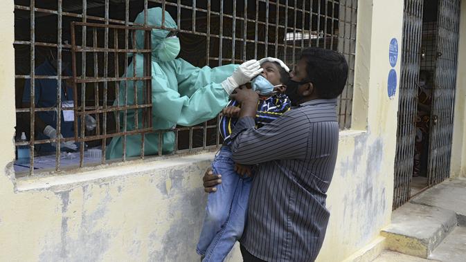 Seorang pria menggendong putranya saat petugas kesehatan mengumpulkan sampel usap untuk menguji virus corona Covid-19 di daerah kumuh di Hyderabad (23/9/2020). Korban meninggal karena Covid-19 di India mencapai 90.000 lebih. (AFP/Noah Seelam)