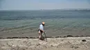 Seorang wanita berjalan di sepanjang pantai di Thessaloniki, Yunani utara (23/6/2021).  Yunani bersiap menghadapi gelombang panas pertama musim panas, mendorong suhu siang hari ke wilayah 40+ Celcius di banyak bagian negara. (AFP/ Sakis Mitrolidis)