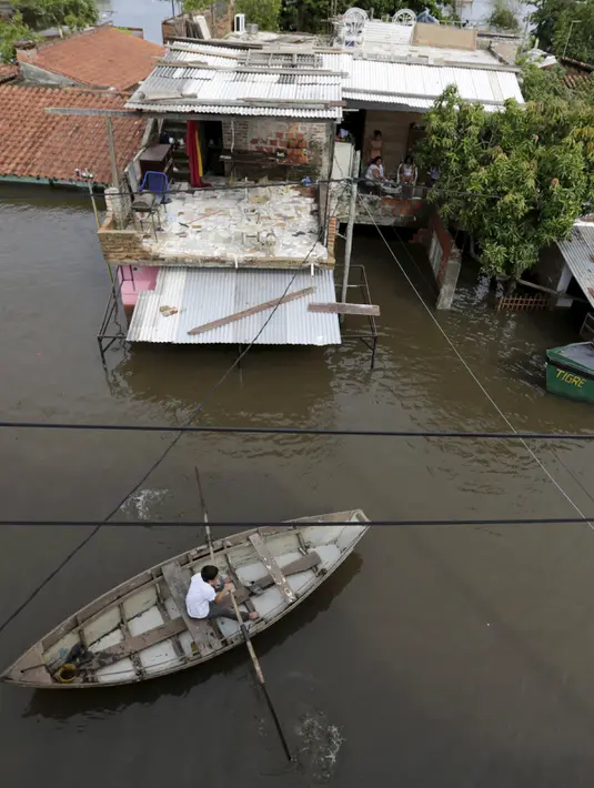 Warga menggunakan perahu melintasi genangan banjir yang merendam Asuncion, Paraguay, Senin (28/12). Banjir terparah dalam kurun waktu 23 tahun ini, bahkan telah membuat lebih dari 100.000 warga mengungsi. (REUTERS/Jorge Adorno)