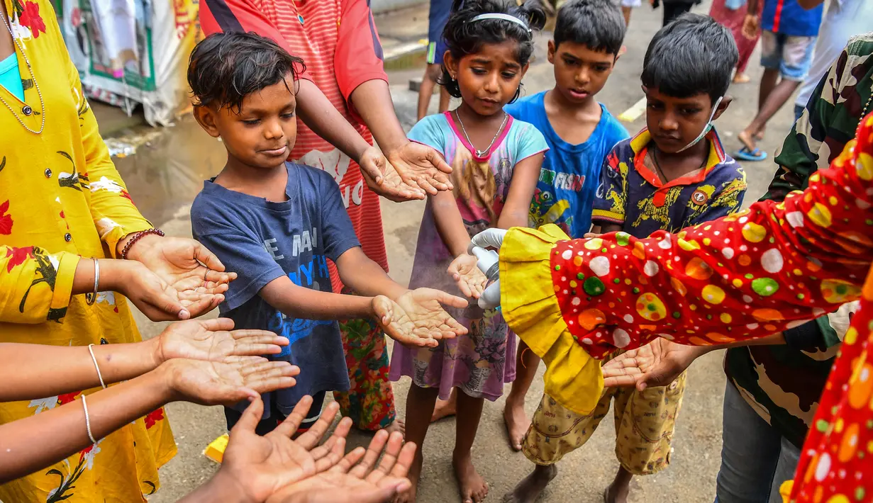 Relawan pekerja sosial Ashok Kurmi, berpakaian seperti badut, menyemprotkan hand sanitiser kepada anak-anak di daerah kumuh Mumbai pada 2 Juni 2021. Kurmi turun tangan memerangi Corona COVID-19 di daerah kumuh Mumbai menggunakan aksesori yang tidak biasa, yaitu kostum badut. (INDRANIL MUKHERJEE/AFP)