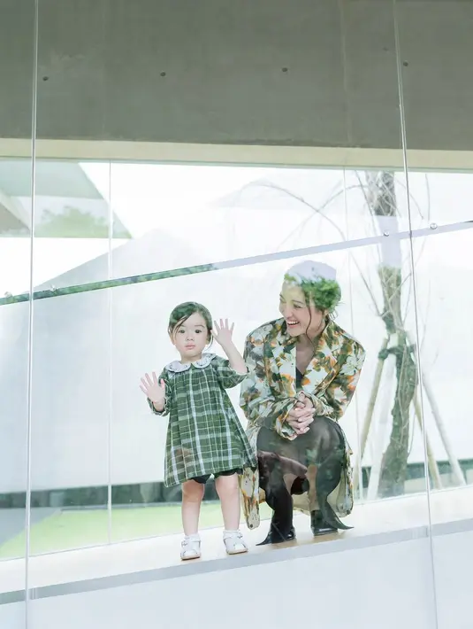 Dengan nuansa hijau, gayanya begitu menggemaskan. Sang anak kenakan dress bersiluet klasik disertai motif tartan yang menggemaskan. [Foto: Instagram/ Julie Estelle]