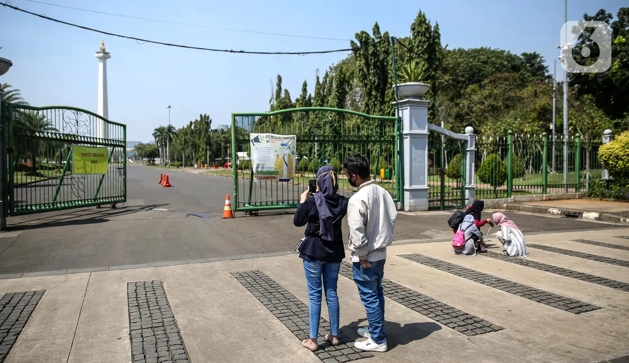 Sejumlah warga mengambil gambar dari depan kawasan Monumen Nasional (Monas), Jakarta, Minggu (26/7/2020). Sejumlah warga mulai mengunjungi kawasan Monas meski masih ditutup sementara di masa PSBB transisi. (Liputan6.com/Faizal Fanani)