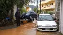 Mobil-mobil menumpuk saat warga menyeberang jalan melalui air banjir setelah hujan lebat di desa Malia, pulau Kreta, Yunani, Selasa (10/11/2020). Banjir merusak jalan, membanjiri ratusan rumah, dan menyeret mobil ke laut di tengah hujan deras yang sedang berlangsung. (AP Photo/Harry Nakos)
