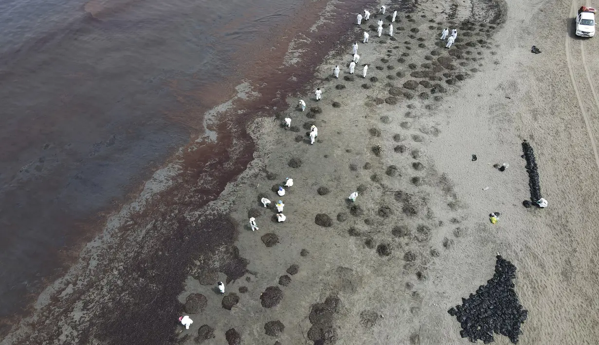 Pekerja mengenakan pakaian pelindung membersihkan Pantai Conchitas yang terkontaminasi tumpahan minyak, di Ancon, Peru, Kamis (20/1/2022). Tumpahan minyak di pantai Peru disebabkan oleh gelombang dari letusan gunung berapi bawah laut di negara Pasifik Selatan Tonga. (AP Photo/Martin Mejia)