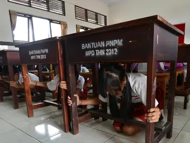 Sejumlah siswa SD berlindung di bawah meja selama latihan tsunami di Tanjung Benoa dekat Denpasar di pulau resor Bali (15/8). (AFP Photo/ Sonny Tumbelaka)
