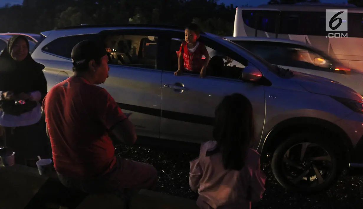 Pemudik beristirahat sembari menyantap makanan untuk berbuka puasa di pinggir ruas jalan tol Cipali KM 187, Kabupaten Cirebon, Jawa Barat, Kamis (30/5/2019). Sejumlah pemudik memilih menggunakan bahu jalan ruas tol untuk berbuka puasa karena penuhnya rest area. (Liputan6.com/Herman Zakharia)