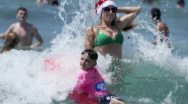 Pengunjung asal Inggris Sophie Woodward (kanan) mengenakan topi Santa saat bermain di air bersama sepupunya Maxi Woodward di Pantai Bondi di Sydney, Senin, 25 Desember 2023. (AP Photo/Rick Rycroft)