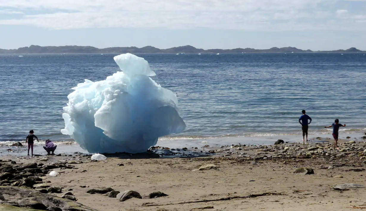 Anak-anak bermain disamping bongkahan es berukuran raksasa di Nuuk, Greenland, 5 Juni 2016. Cuaca ekstrem membuat sebagaian gunung es mencair yang membuat naiknya air laut. (REUTERS / Alister Doyle)