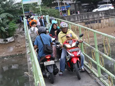 Warga serta pengendara motor menyeberangi Kanal Banjir Barat (KBB) di kawasan Tanah Abang, Jakarta, Jumat (30/12). Tidak tersedianya fasilitas penyeberangan lain membuat warga serta pengendara harus berbagi jalan. (Liputan6.com/Immanuel Antonius)