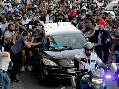 Para penggemar berkerumun di samping mobil jenazah yang membawa mendiang legenda sepak bola Argentina, Diego Maradona menuju pemakaman, di Buenos Aires, Kamis (26/11/2020).  Maradona meninggal dunia dalam usia 60 tahun pada Rabu (25/11) karena serangan jantung. (Raul FERRARI/TELAM/AFP)