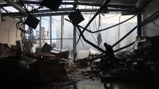 Seorang karyawan toko kelontong, yang hancur akibat serangan rudal Rusia, mengumpulkan barang-barang di Kostyantynivka, wilayah Donetsk, pada 25 Februari 2024. (Anatolii STEPANOV/AFP)