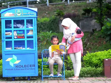 Seorang ibu menemani anaknya membaca buku yang tersedia di layanan Kotak Literasi Cerdas (Kolecer) di Taman Sempur, Bogor, Jawa Barat, Kamis (20/12). Kolecer adalah perpustakaan jalanan gratis. (Merdeka.com/Arie Basuki)