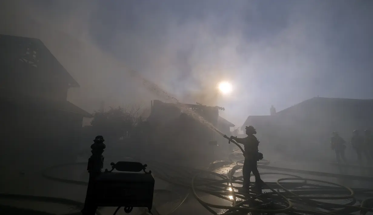 Seorang petugas pemadam kebakaran memadamkan sebuah rumah yang terbakar di Whittier, California (10/2/2022). Kebakaran hutan yang dipicu oleh angin kencang Santa Ana meletus di perbukitan di pantai California Selatan Kamis pagi. (AP Photo/Ringo H.W. Chiu)
