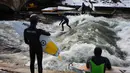 Para peselancar menunggu giliran untuk berselancar di Sungai Eisbach selama musim dingin di Munich, Jerman, 4 Januari 2017. Sungai Eisbach merupakan salah satu tempat berselancar sungai yang paling populer di kota Munich. (Mark RALSTON/AFP)
