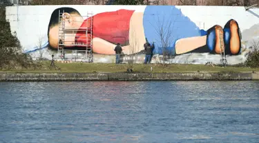 Seniman melukis mural bergambar balita Aylan Kurdi yang meninggal karena tenggelam di dinding pinggiran sungai di Frankurt, Jerman, 9 Maret 2016. Gambar tersebut dibuat untuk menarik simpati pengendara, wisatawan dan dunia. (Arne Dedert/dpa/AFP)