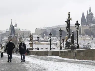 Orang-orang menyeberangi Jembatan Charles abad pertengahan setelah hujan salju pertama di Praha, Republik Ceko (3/12/2020). (AP Photo / Petr David Josek)