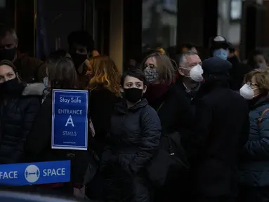 Orang-orang mengantre mengenakan masker melawan virus corona, di luar teater untuk pertunjukan Les Miserables di London, Selasa (28/12/2021). Di Inggris, pemerintah telah mengatakan bahwa tidak akan ada pembatasan baru sebelum Tahun Baru. (AP Photo/Alastair Grant)