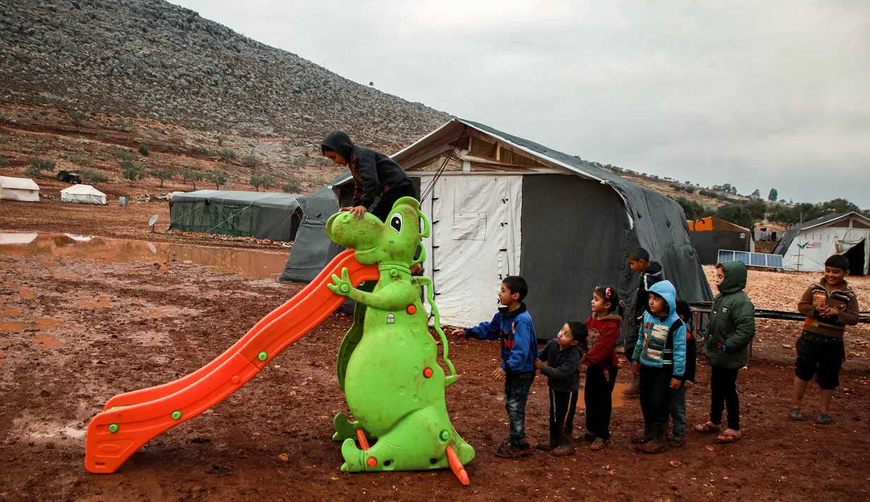 Anak-anak mengantre untuk bermain perosotan turun di sebuah kamp untuk warga Suriah yang kebanjiran di dekat desa Killi di utara provinsi Idlib barat laut (5/12/2019). (AFP Photo/Aaref Watad)