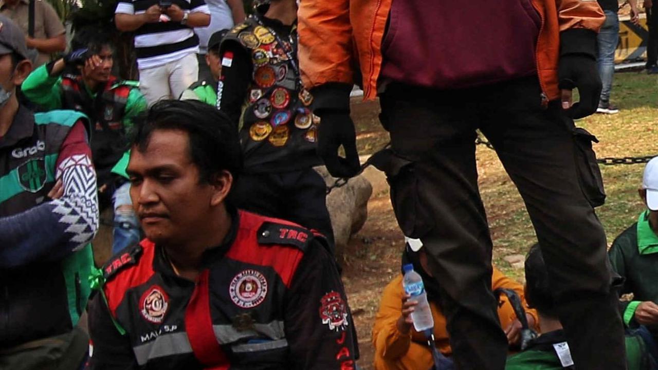 Massa Ojol berdiri di atas barikade beton saat berunjuk rasa di Jalan Medan Merdeka Barat di kawasan Patung Kuda.