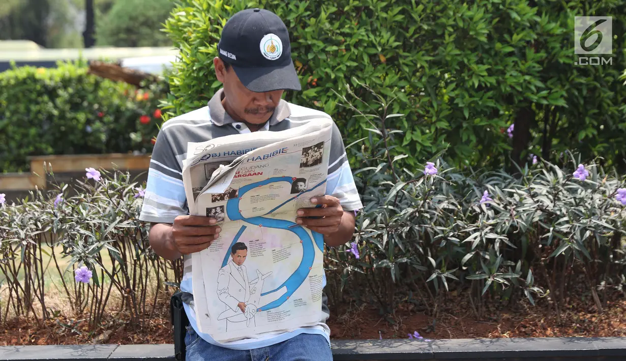 Warga membaca koran di TMP Kalibata untuk melihat prosesi pemakaman Presiden RI ke-3 BJ Habibie, Jakarta, Kamis (12/9/2019). BJ Habibie wafat pada Rabu (11/9) di usia 83 tahun. (Liputan6.com/Helmi Fithriansyah)