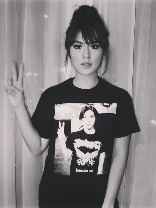 Glamour dan elegan, gaya berbusana yang biasa melekat di tubuh Raisa setiap kali di panggung. Namun kali ini, ia tak kalah cantik saat memakai kaos hitam yang ternyata bergambar wajahnya sendiri. (Instagram/6690)