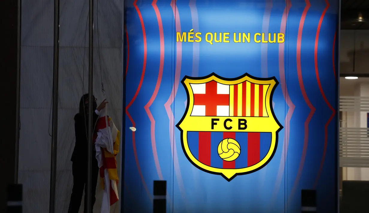 Seorang pekerja menurunkan bendera institusi dan klub sebelum kantor Barcelona tutup pada hari itu di stadion Camp Nou di Barcelona, Spanyol, Kamis (5/8/2021). Barcelona pada Kamis 5 Agustus 2021 bahwa Lionel Messi tidak akan bertahan dengan klub. (AP Photo/Joan Monfort)
