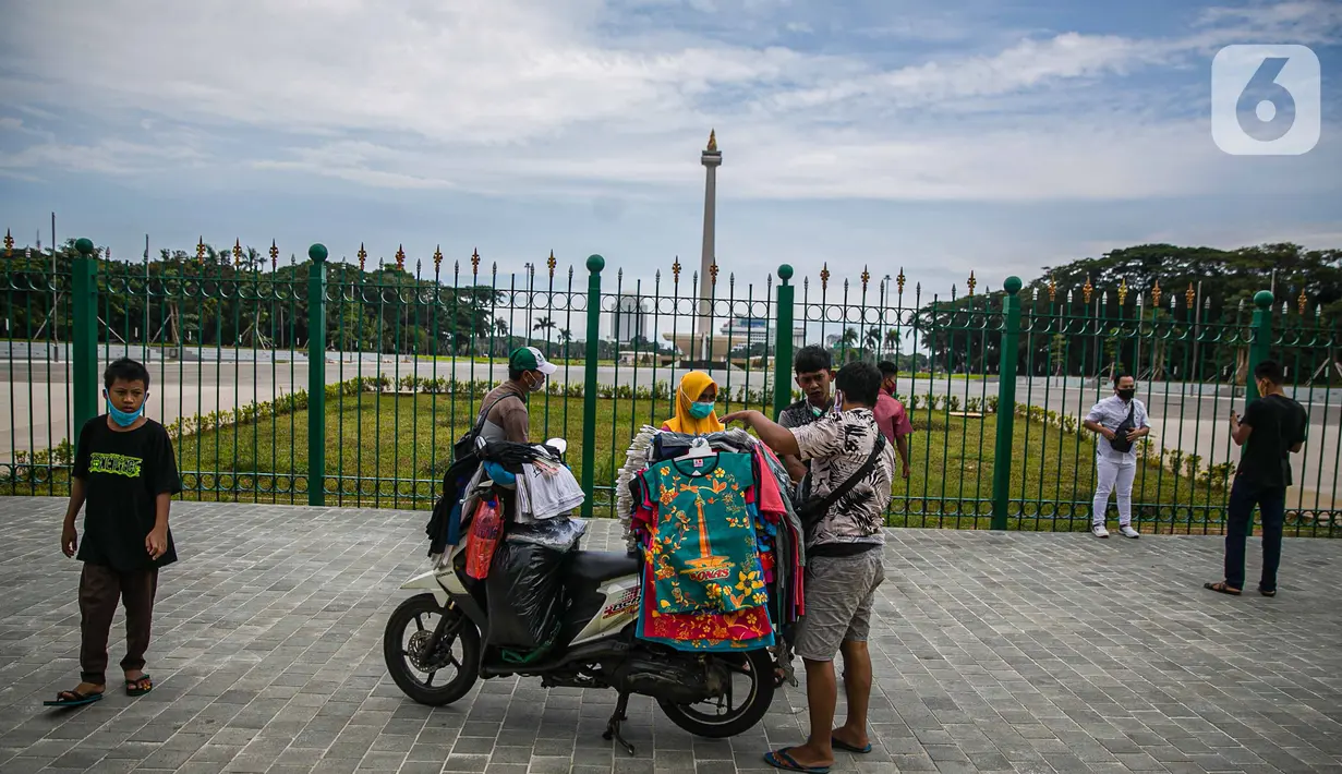 Pedagang kaos cendera mata keliling mencoba peruntungan dari para pengunjung yang ingin menyaksikan Tugu Monas Jakarta dari balik pagar, Sabtu (2/1/2021). (Liputan6.com/Faizal Fanani)