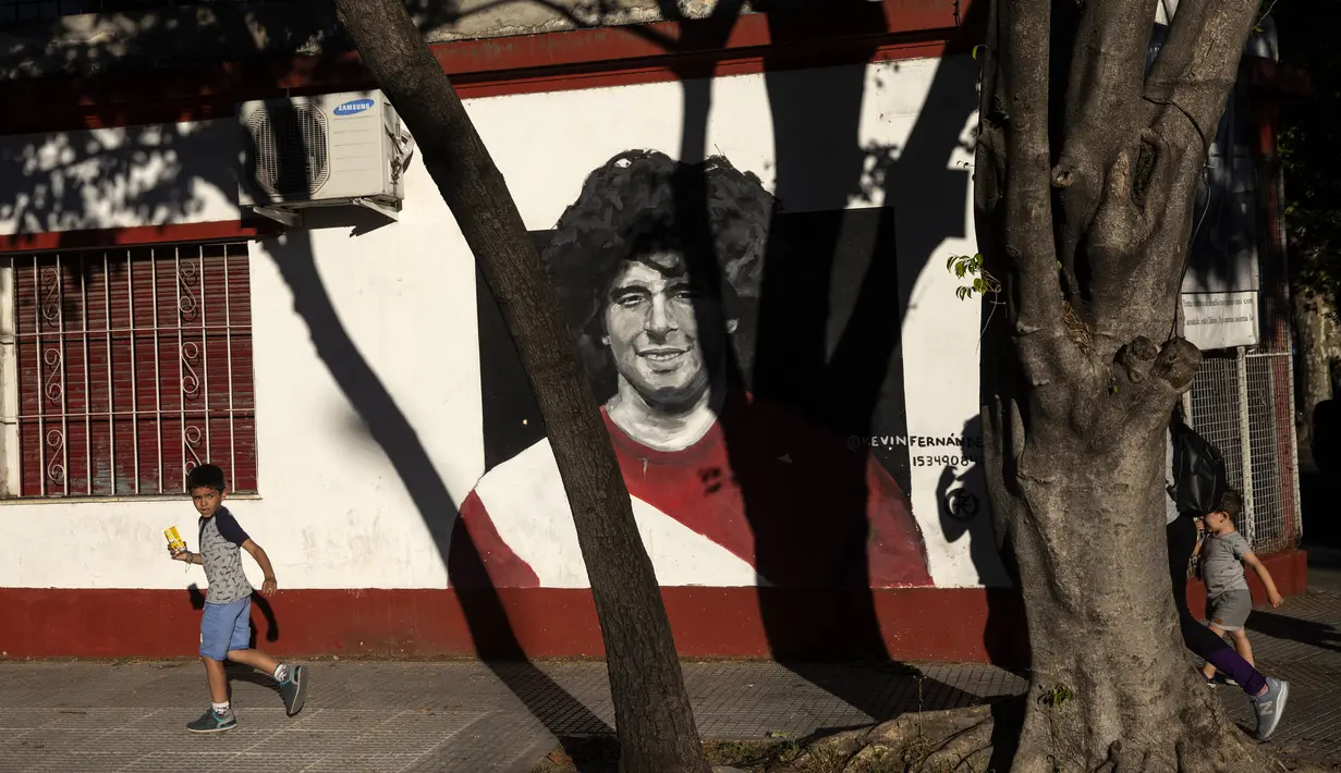 Seorang pemuda berjalan melewati mural mendiang legenda sepak bola dunia, Diego Maradona di dekat stadion Argentinos Juniors di Buenos Aires, Argentina, Selasa (23/11/2021). Peringatan pertama kematian Maradona digelar pada 25 November 2021. (AP Photo/Rodrigo Abd)