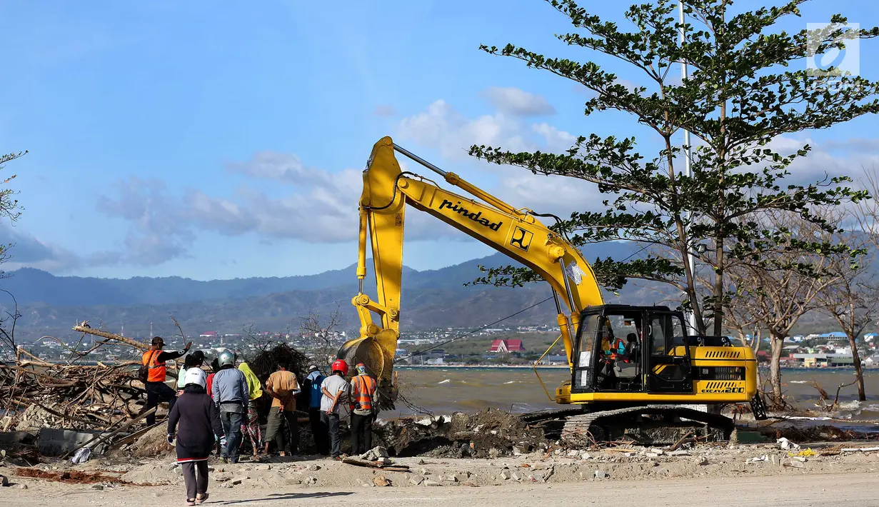 Warga menyaksikan proses evakuasi Nanang Kosim (20) menggunakan alat berat, yang diduga masih tertimbun di dalam tanah pascagempa dan tsunami Palu di Pantai Talise, Sulawesi Tengah, Senin (8/10). (Liputan6.com/Fery Pradolo)