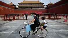 Seorang perempuan mengendarai sepedanya dengan seorang anak duduk di kursi belakang melewati Kota Terlarang di Beijing, China, Selasa (7/6/2022). Pemerintah melonggarkan beberapa pembatasan Covid-19 dengan sebagian besar museum gedung bioskop, dan pusat kebugaran diizinkan beroperasi hingga 75 persen dari kapasitas. (WANG Zhao / AFP)
