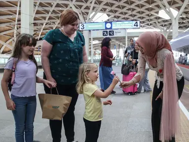 Petugas perempuan Kereta Cepat Whoosh mengenakan kebaya sambil membagikan bunga kepada calon penumpang di Stasiun Halim Whoosh, Jakarta, Senin (21/4/2025). (Liputan6.com/Angga Yuniar)