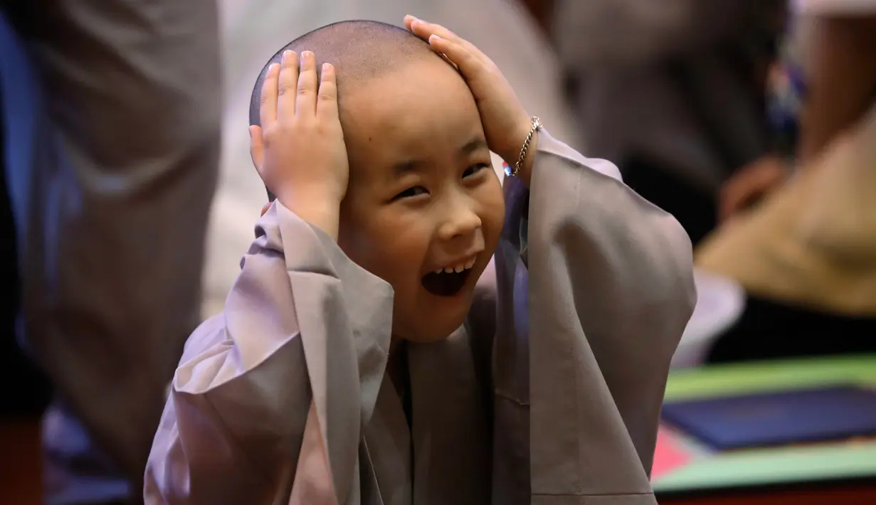 Seorang anak lelaki tertawa memegang kepalanya usai dicukur pada seremonial ulang tahun Buddha di kuil Jogye, Seoul, Rabu (2/5). Sepuluh anak terpilih mendapatkan pengalaman menjadi biksu dalam rangkaian acara peringatan hari lahir Buddha (AP/Lee Jin-man)