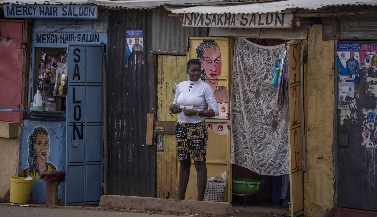 <p>Seorang perempuan berdiri di luar sebuah salon di daerah Kibera di Nairobi, Kenya, Kamis, 11 Agustus 2022. Rakyat Kenya menunggu hasil pemilihan presiden yang berlangsung ketat namun tenang di mana jumlah pemilih lebih rendah daripada biasanya. (AP Photo/Ben Curtis)</p>