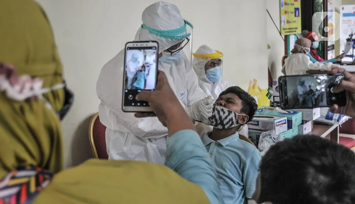 Orang tua mendampingi anaknya saat menjalani tes Covid-19 di GOR Kecamatan Makasar, Jakarta, Senin (17/5/2021). Pemkot Jakarta Timur menggelar tes Covid-19 gratis bagi warga yang baru tiba di Ibu Kota guna mencegah penyebaran virus Corona usai mudik. (merdeka.com/Iqbal S Nugroho)