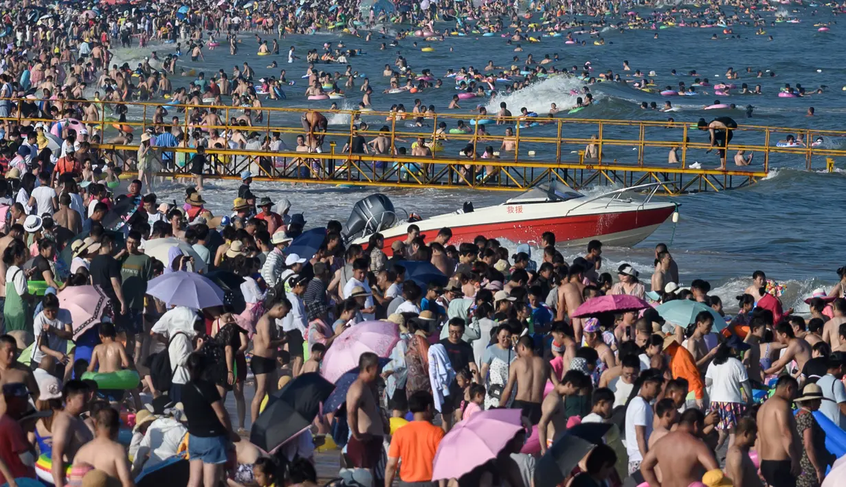 Wisatawan mengunjungi pantai sambil mendinginkan diri di Qingdao, China timur, pada 3 Agustus 2019. Banyak warga di Negeri Tirai Bambu memanfaatkan musim panas dengan mengunjungi pantai untuk mengisi liburan. (Photo by FRED DUFOUR / AFP)