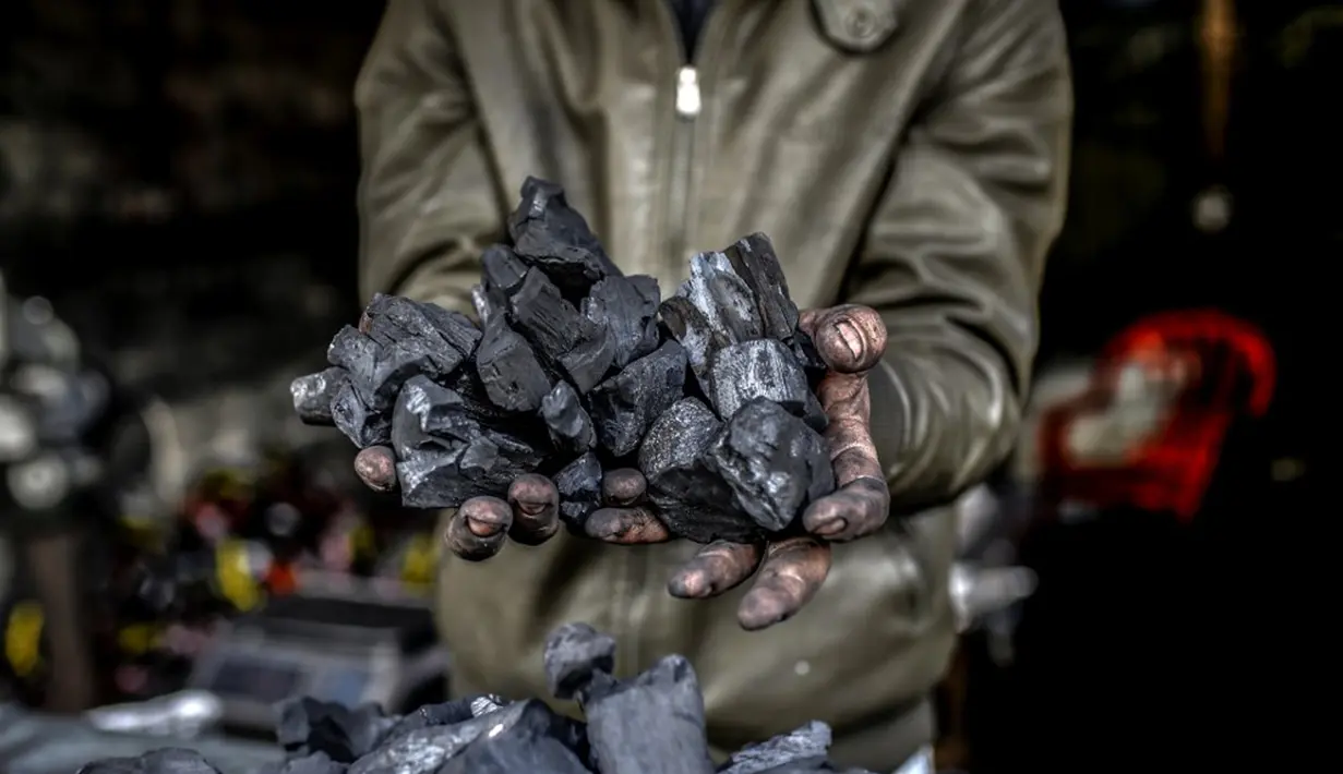 Seorang pekerja menunjukkan segenggam arang di fasilitas produksi arang al-Hattab, sebelah timur Kota Gaza, Palestina, 28 Januari 2021. Satu kilogram arang dijual seharga USD 1,50 di tempat dan USD 2,50 di pasar. (Mohammed ABED/AFP)