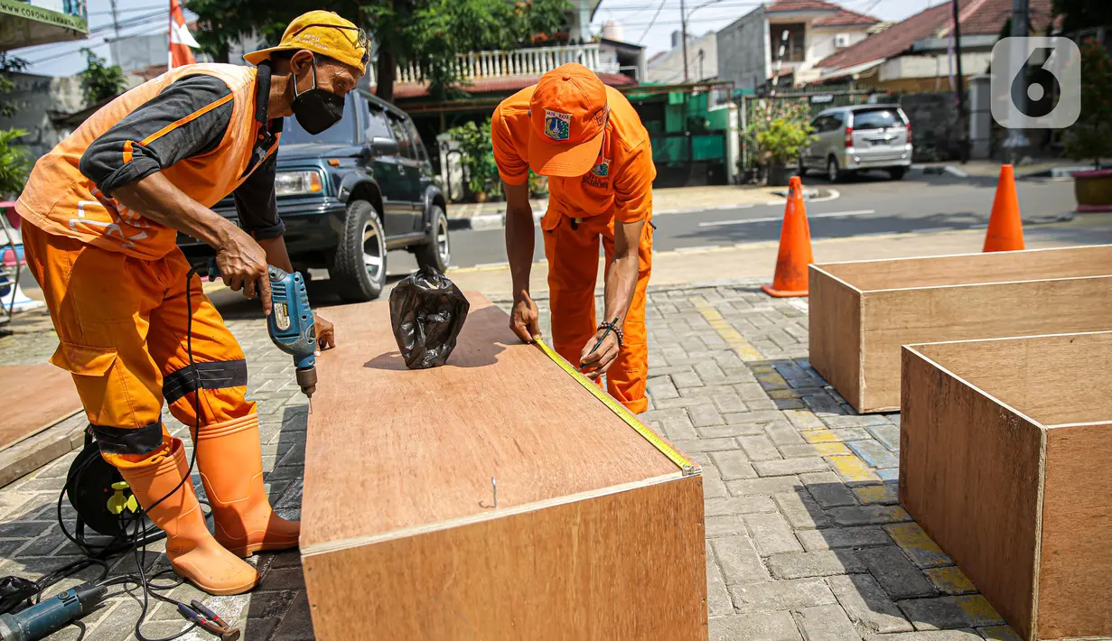 Petugas PPSU memproduksi peti jenazah di halaman Kantor Kelurahan Kayu Putih, Jakarta, Selasa, (6/7/2021). Kelurahan Kayu Putih berinisiatif membuat peti jenazah dilatar belakangi warganya yang terkendala ketersediaan peti saat angka kematian COVID-19 meningkat di DKI. (Liputan6.com/Faizal Fanani)