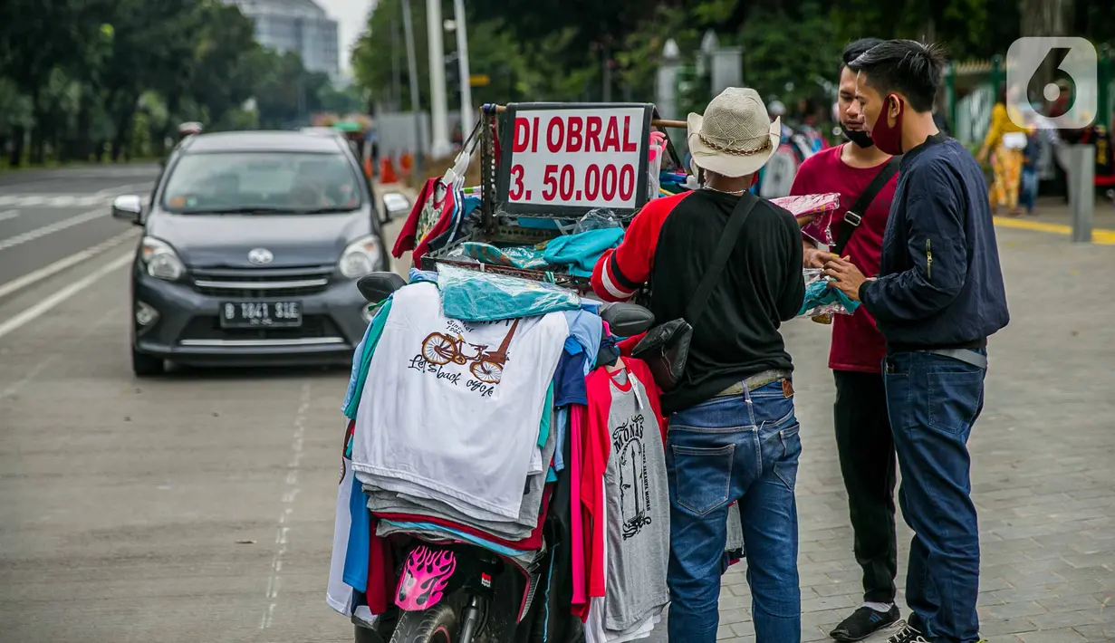 Pedagang kaos cendera mata keliling berinteraksi dengan wisatawan kawasan Monas, Jakarta, Sabtu (2/1/2021). Sejumlah tempat wisata dan taman terbuka yang dikelola Pemprov DKI ditutup selama hari Natal dan Tahun Baru. (Liputan6.com/Faizal Fanani)
