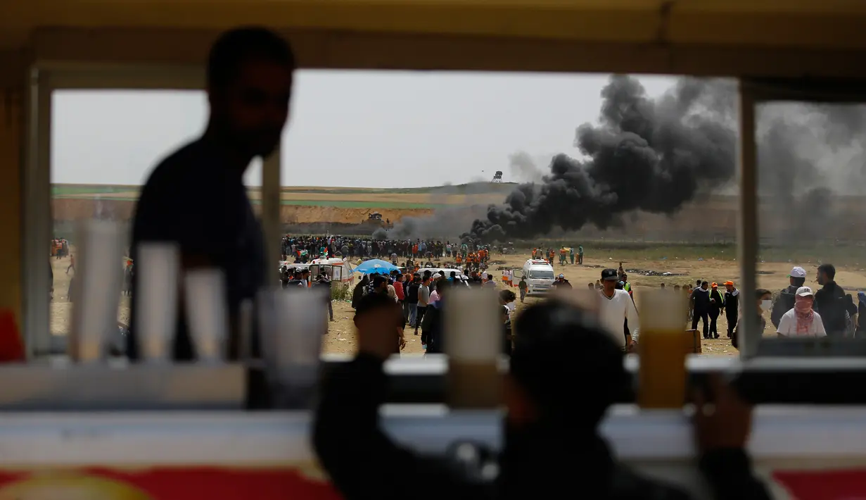 Warga Palestina membakar ban hingga menimbulkan asap tebal di perbatasan Palestina-Israel di kota Gaza tengah (13/4). Mereka melakukan aksi tersebut menyusul tewasnya 33 orang Palestina akibat serangan tentara Israel. (AFP/Mohammed Abed)