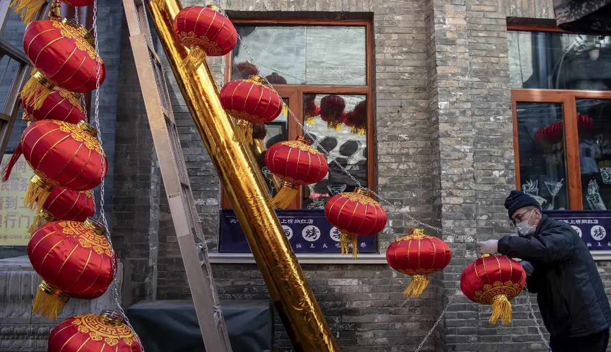 Seorang pekerja memasang lentera tradisional Tiongkok di sepanjang gang menjelang Tahun Baru Imlek di Beijing, China, 2 Februari 2021. Imlek tahun ini jatuh pada tanggal 12 Februari 2021. (NOEL CELIS/AFP)