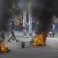 Seorang pria menambahkan puing-puing untuk dibakar di barikade ban yang terbakar yang dipasang oleh pengunjuk rasa selama demonstrasi menuntut Perdana Menteri Haiti Ariel Henry mundur dan menyerukan kualitas hidup yang lebih baik, di Port-au-Prince, Haiti, Senin (29/8/2022). (AP Photo/Odelyn Joseph)
