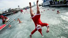 Seorang peserta dalam kostum sinterklas melompat ke air saat  kompetisi renang Copa Nadal di Port Vell Barcelona, Selasa (25/12). Lomba tradisional ini sudah menjadi tradisi lama yang mereka lakukan tiap tahun pada hari natal. (Josep LAGO / AFP)