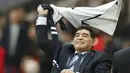 Diego Armando Maradona mengibarkan jersey Tottenham Hotspur saat mengyaksikan laga Premier Leagu antara Tottenham melawan Liverpool di Wembley Stadium, London, (22/10/2017). (AP/Frank Augstein)