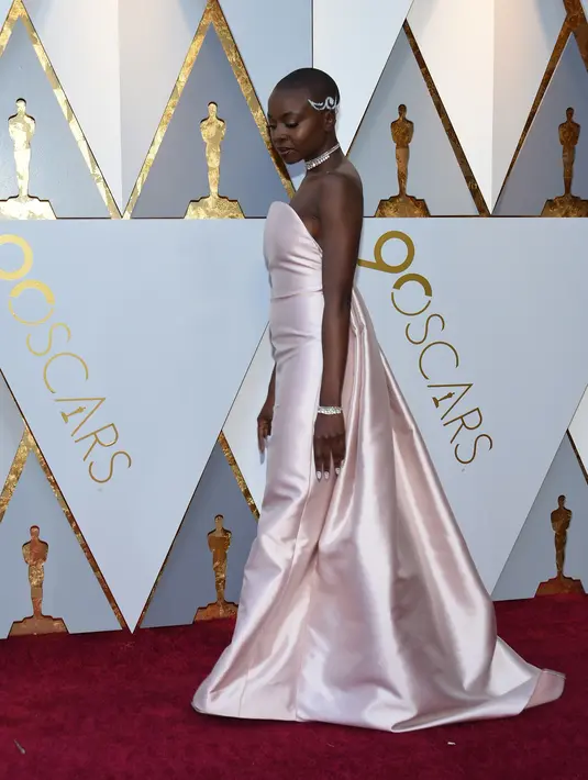 Aktris Danai Gurira berpose di karpet merah ajang Piala Oscar 2018, Los Angeles, Minggu (4/3).  Pemeran Okoye dalam film "Black Panther" ini tampil stunning dengan gaun merah muda sederhana beserta aksesori silver di tubuhnya. (VALERIE MACON / AFP)